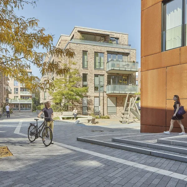 Menschen, die ihren Alltag an einem sonnigen Tag in einem von FRANK ganzheitlich entwickelten Wohnquartier verbringen.